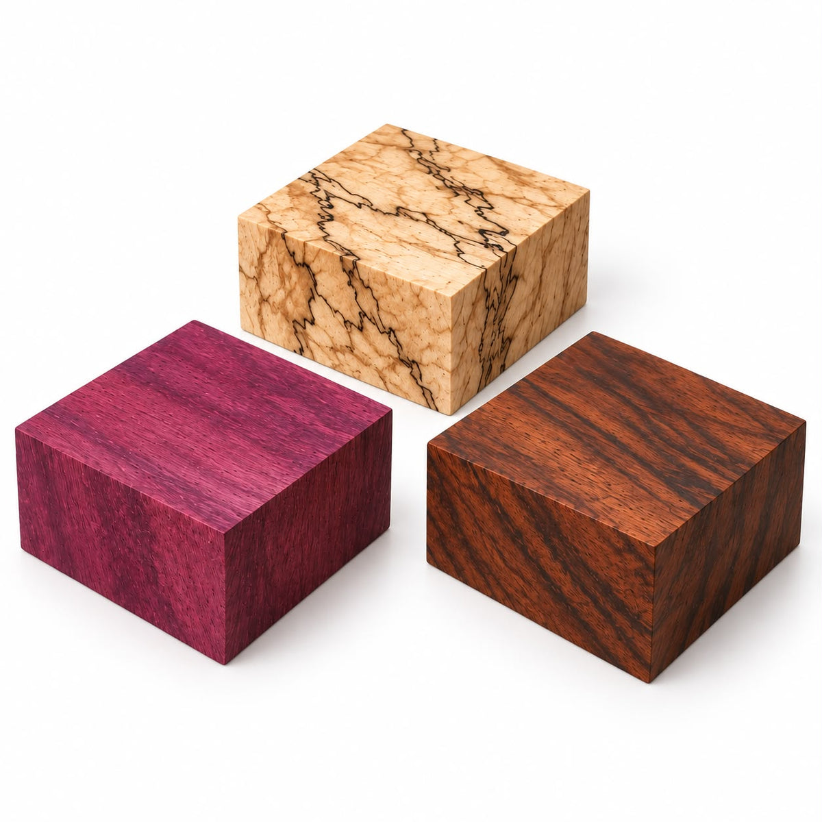 Three square wooden blocks with distinct wood grain patterns, displayed on a clean white background. One block is a vibrant magenta-pink, another is a warm light tan with dark brown veining, and the third is a rich dark reddish-brown.
