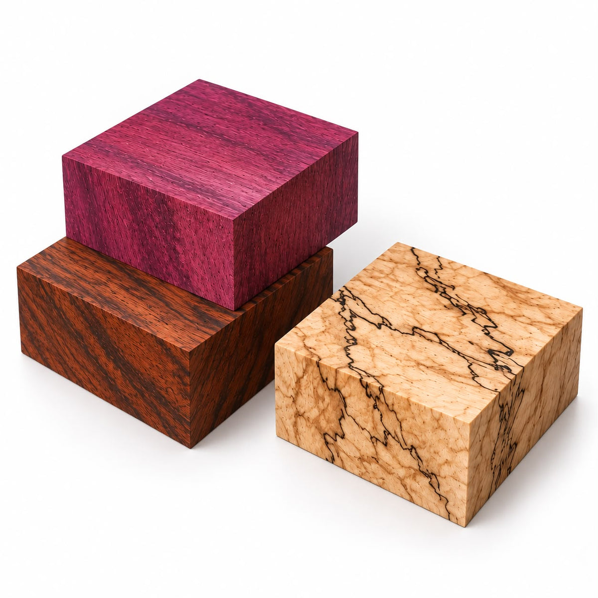 Three 6x6x2 inch kiln-dried exotic wood bowl blanks arranged with wood curls and green leaves, highlighting the deep purple tone of Purpleheart, ink-like lines of Spalted Tamarind, and rich reddish-brown grain of Granadillo.