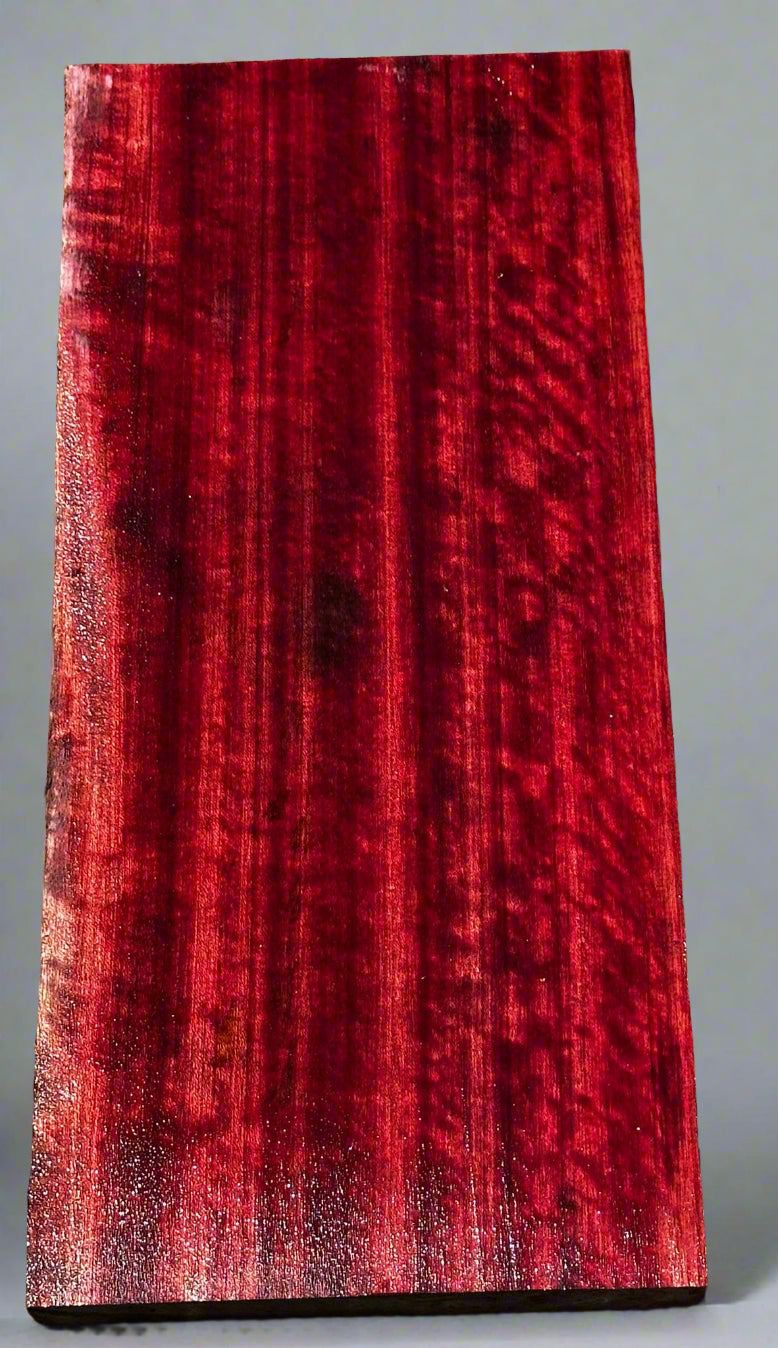 Red wood sample with visible grain on a gray surface